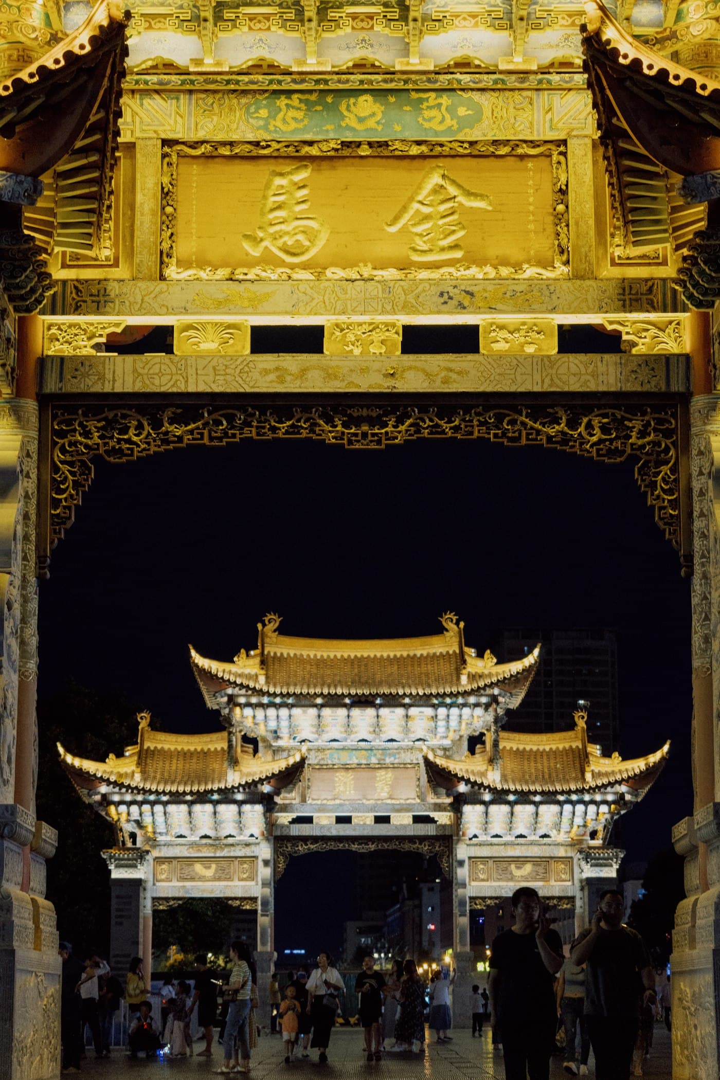 A golden gateway in Kunming with people walking beneath it